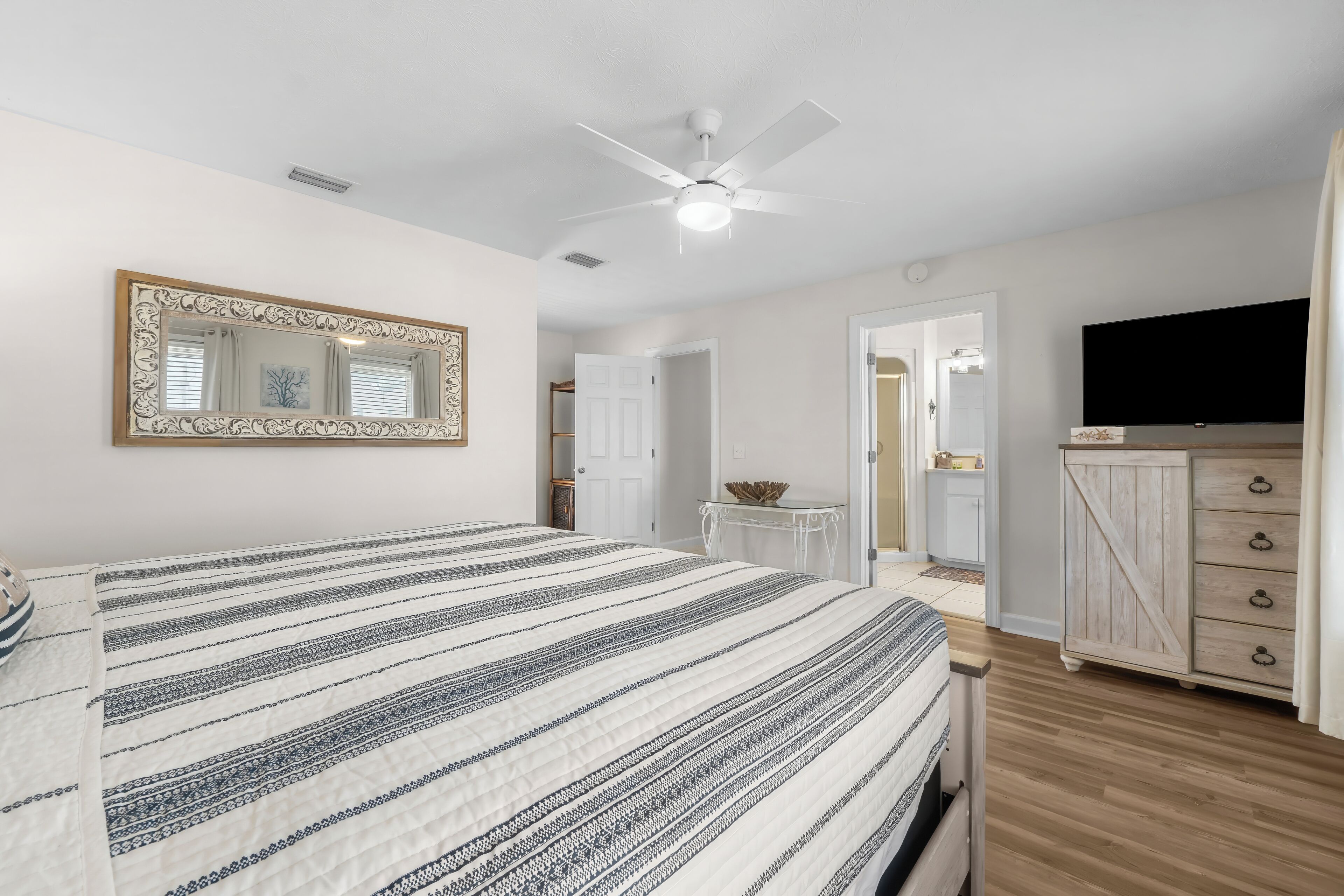 Un dormitorio con cama, ventilador de techo, televisor y cómoda.