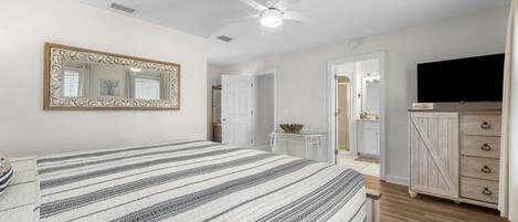 Un dormitorio con cama, ventilador de techo, televisor y cómoda.