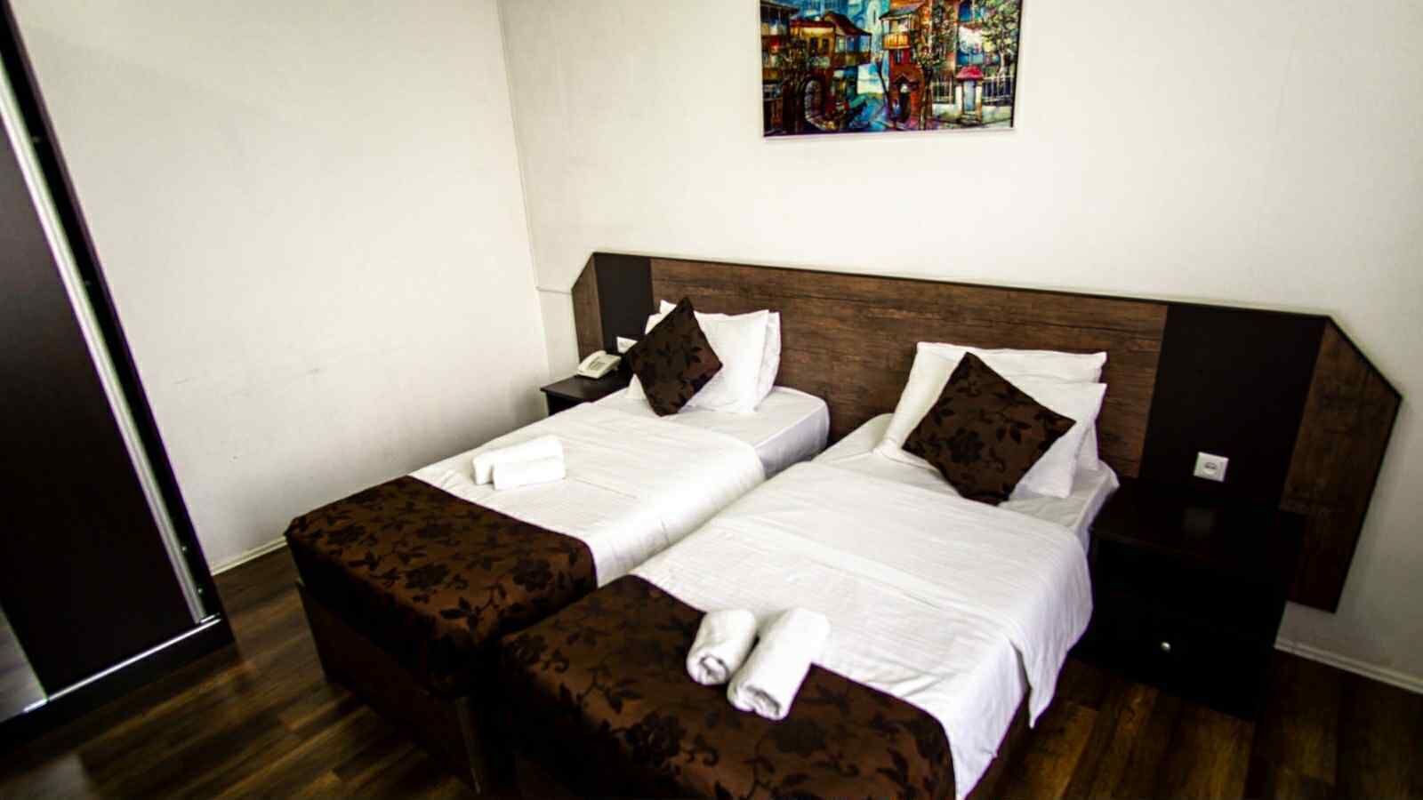 A hotel room with two beds, a wooden headboard, a painting on the wall, and a telephone on the nightstand.