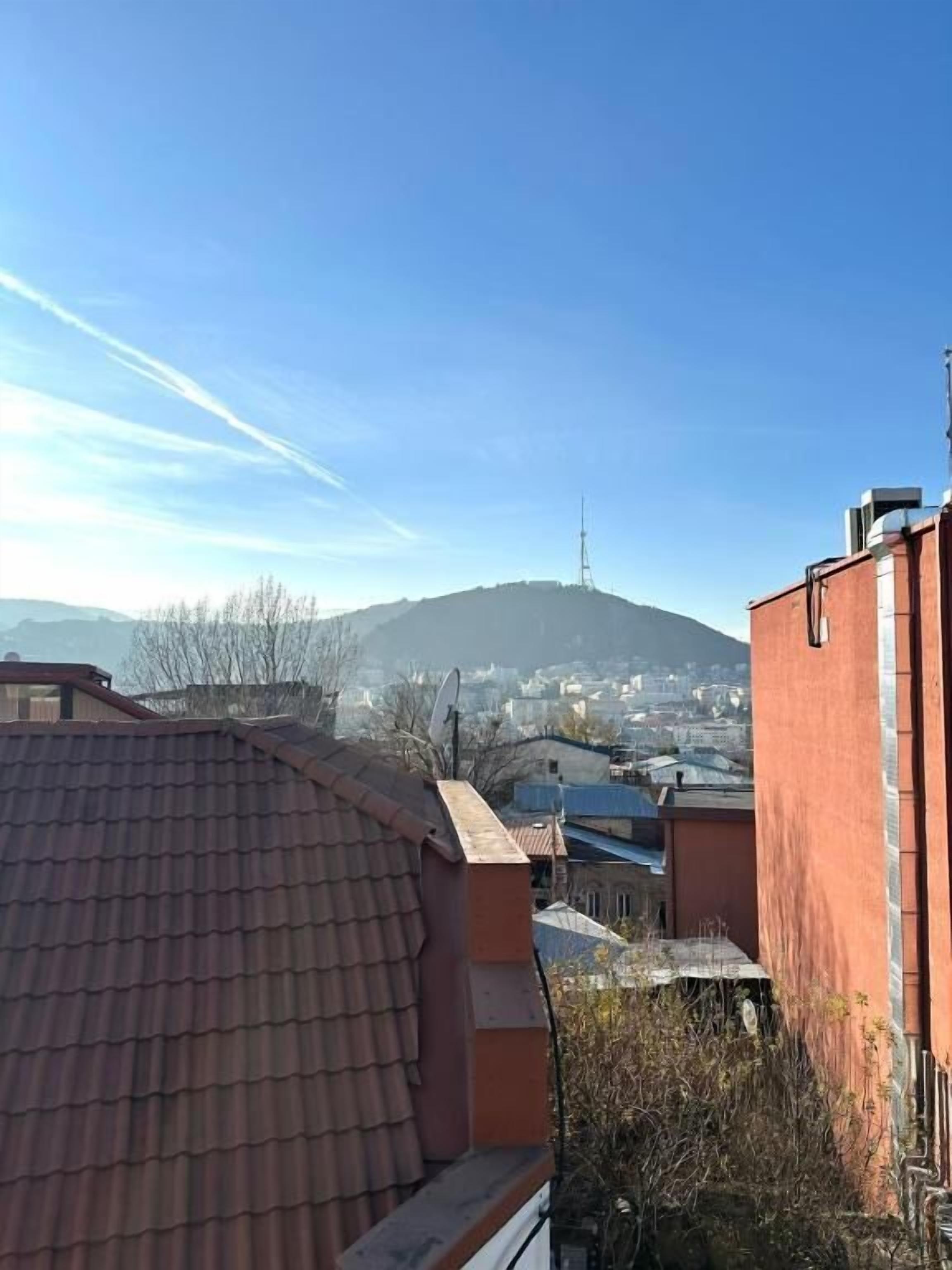 A building with a sloped roof, a satellite dish, and a view of a cityscape with a hill in the background.