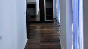 Un couloir avec un plancher en bois, un luminaire au plafond, une porte coulissante et une fenêtre avec des rideaux.