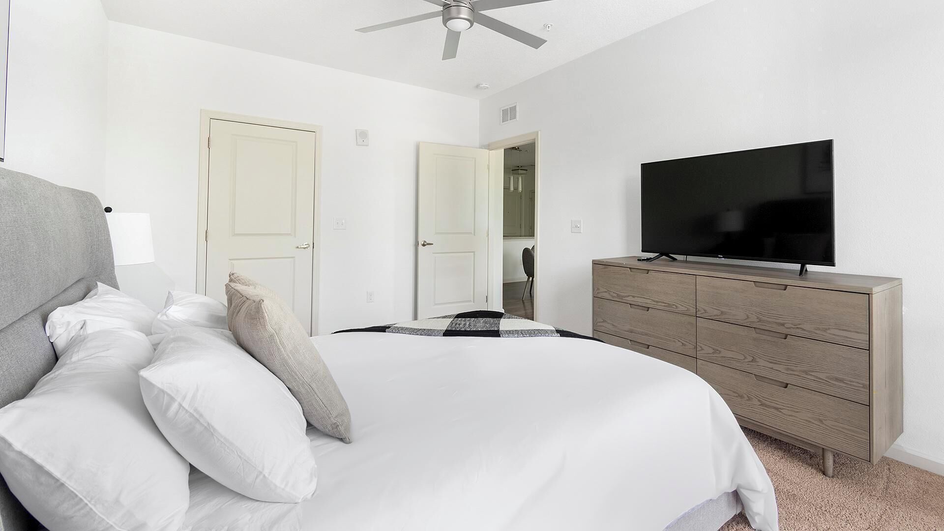 A bedroom with a bed, a television on a wooden dresser, and two doors leading to other rooms.