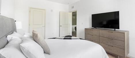 A bedroom with a bed, a television on a wooden dresser, and two doors leading to other rooms.