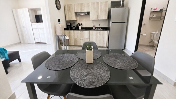 A modern kitchen with a refrigerator, microwave, and stove. There is a dining table with four chairs and a clock on the wall. - CABO DOWNTOWN STUDIOS: Cozy Queen Studios Walk to Marina #5 (Cabo San Lucas)