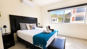 A bedroom with a bed, a nightstand, a window, and an air conditioning unit. - CABO DOWNTOWN STUDIOS: Cozy Queen Studios Walk to Marina #5 (Cabo San Lucas)