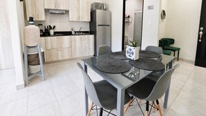A modern kitchen with light wood cabinets, a stainless steel refrigerator, and a dining area with a glass table and grey chairs. - CABO DOWNTOWN STUDIOS: Cozy Queen Studios Walk to Marina #5 (Cabo San Lucas)