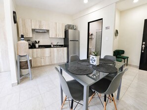 A modern kitchen with light wood cabinets, a stainless steel refrigerator, and a dining area with a glass table and grey chairs. - CABO DOWNTOWN STUDIOS: Cozy Queen Studios Walk to Marina #5 (Cabo San Lucas)
