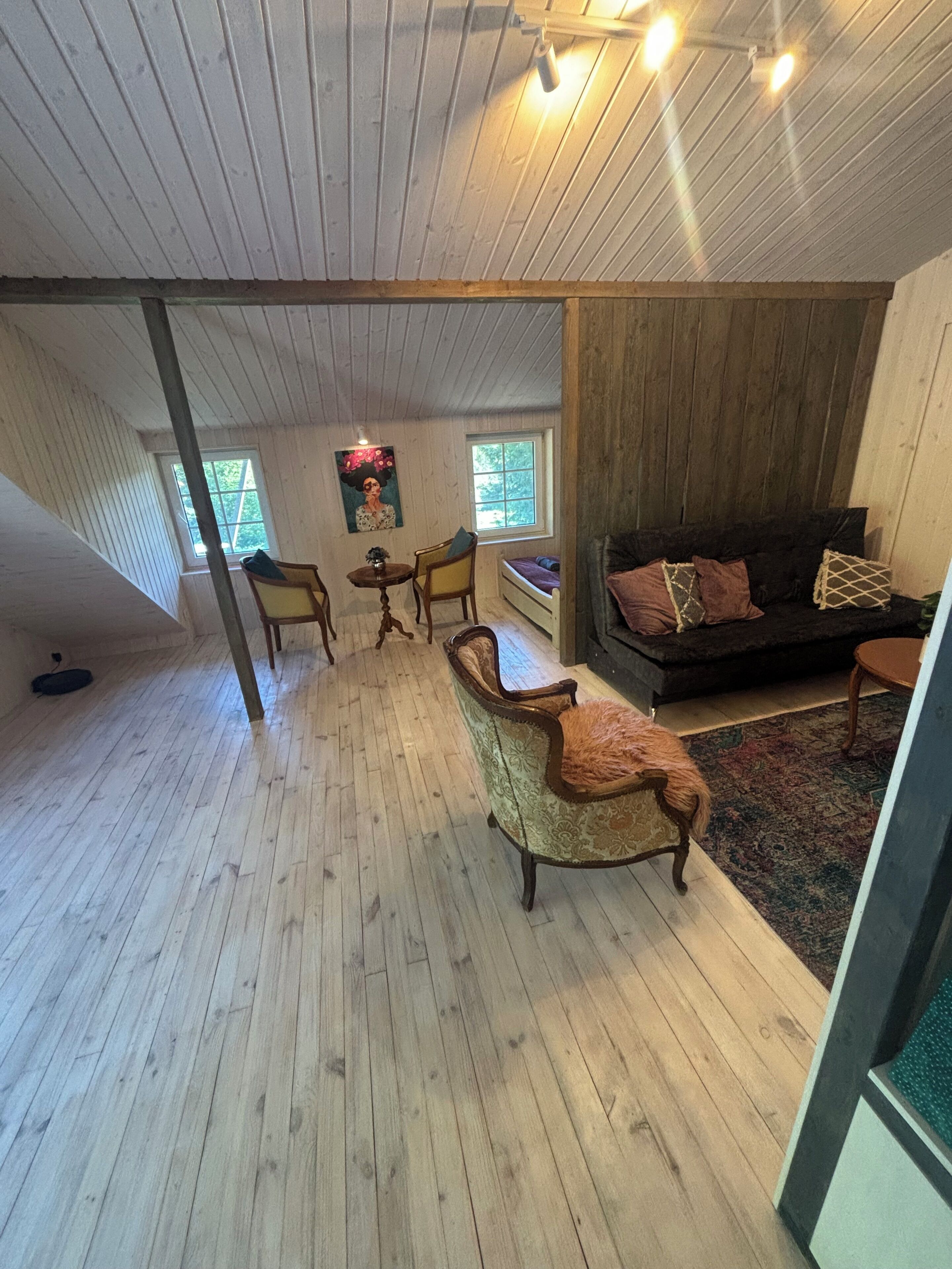 Une pièce de style loft avec un plancher en bois, un canapé, une table à manger avec des chaises et une fenêtre donnant sur un paysage agréable.