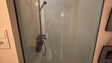 A glass-enclosed shower with a handheld showerhead and a wall-mounted control.
