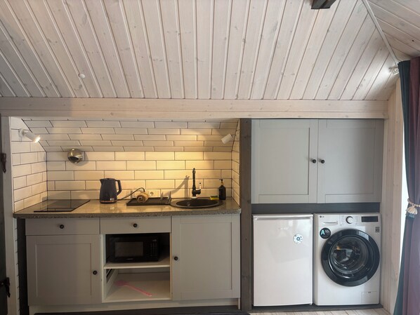 A compact kitchen with a microwave, sink, and washing machine.