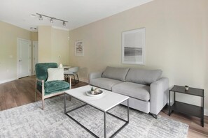 A living room with a green armchair, grey sofa, white coffee table, and a small side table with a plant. - Landing | Spectacular 1BD, Clubhouse, Gym (Hyattsville)