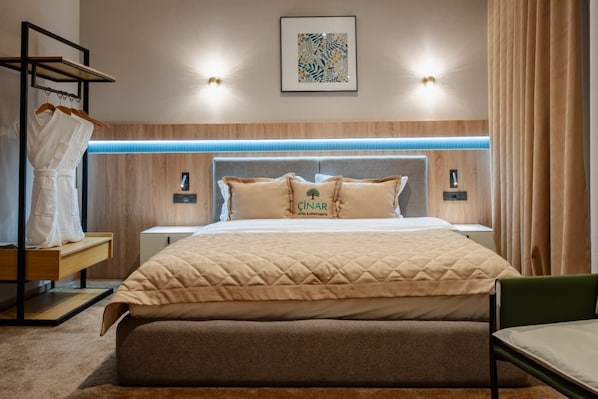 Habitación de hotel con cama, mesitas de noche, perchero y un cuadro en la pared.