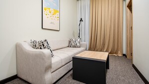 Een moderne woonkamer met een bank, een salontafel, een lamp en een groot raam met gordijnen.