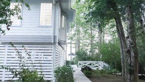 A white building with a covered porch, surrounded by trees and a wooden deck. - Bayfront Retreat on 1.5 Acres - Private Dock - 4BR Near Destin (Freeport)