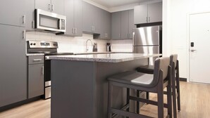 A modern kitchen with grey cabinets, stainless steel appliances, a central island with bar stools, and a white door. - Landing | Beautiful 2BD, Courtyard, Gym (St. Louis)