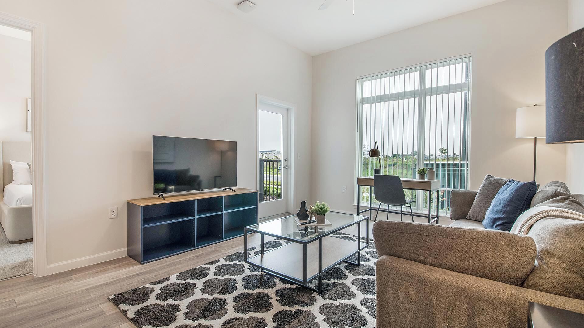 A modern living room with a flat-screen TV, a glass coffee table, a sofa, and a large window with a view.