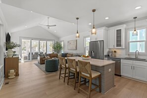 Una cocina moderna con una isla central, iluminación colgante y un área de comedor con un sofá y sillas.
