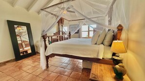 Ein Bett mit Himmelbett, ein Nachttisch aus Holz mit Lampe und ein großer Spiegel an der Wand.