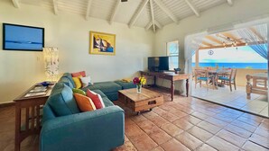 Ein Wohnzimmer mit Sofa, Fernseher und Essbereich mit Blick aufs Meer.