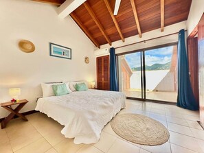 A bedroom with a bed, a nightstand, a window with curtains, a view of the outdoors, and a wooden ceiling.