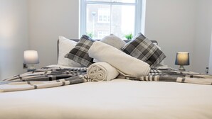 Een opgemaakt bed met een opgerolde handdoek, kussens en een dekbed.
