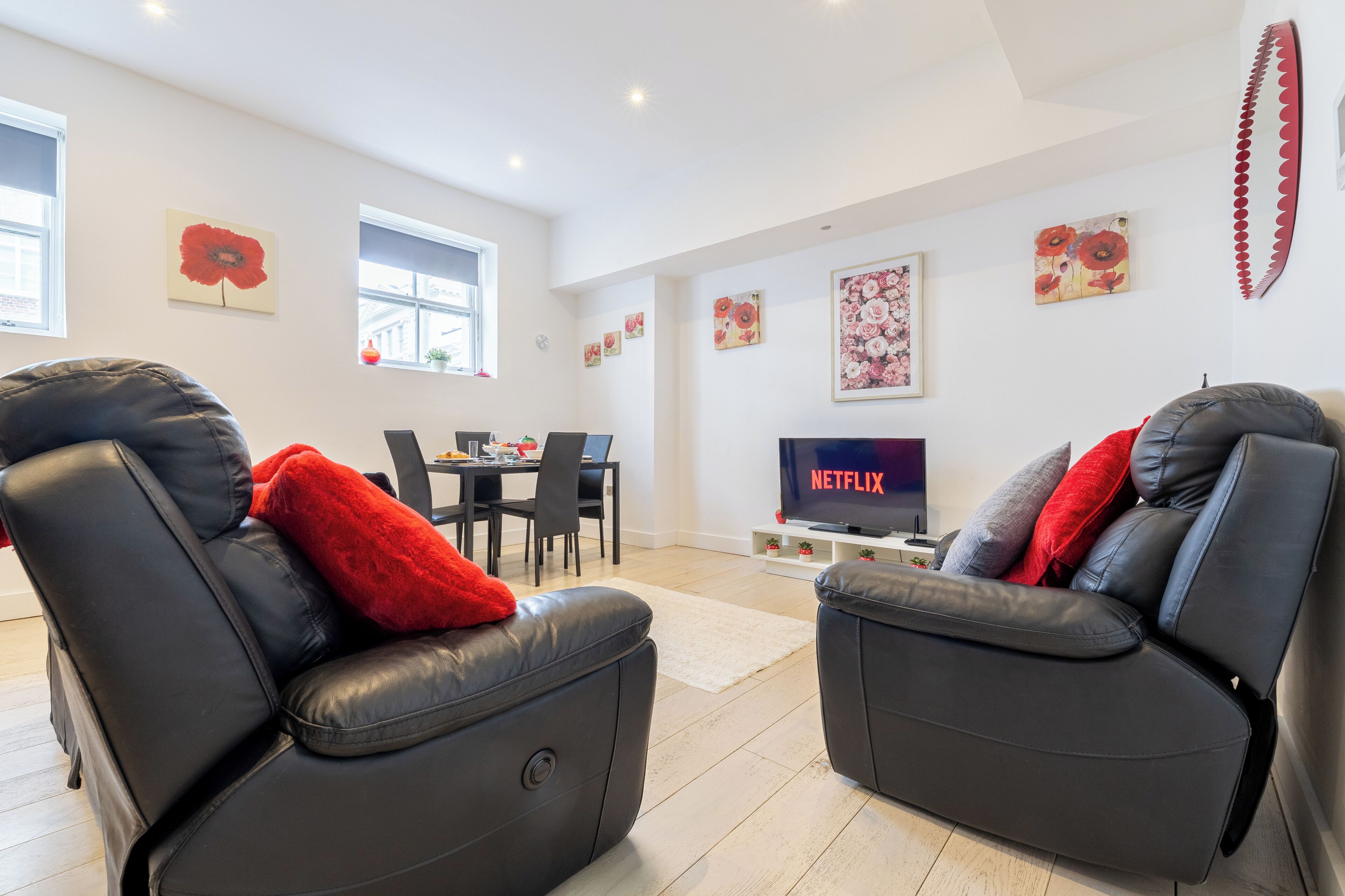 A modern living room with leather recliners, a dining area, and a flat-screen TV displaying 'NETFLIX'.