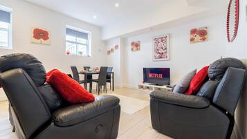A modern living room with leather recliners, a dining area, and a flat-screen TV displaying 'NETFLIX'.