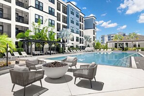 A modern outdoor pool area with lounge chairs, a fire pit, and a covered seating area. - Landing | Modern 1BD, Gym, Pool (Tampa)
