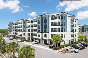A multi-story residential building with a modern architectural design, featuring a parking lot with several cars and palm trees. - Landing | Modern 1BD, Gym, Pool (Tampa)