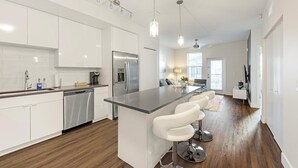 Une cuisine moderne avec des meubles blancs, des appareils en acier inoxydable et un îlot central doté de tabourets de bar.