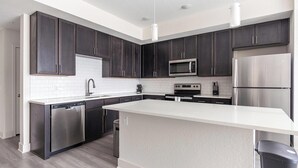 A modern kitchen with dark cabinetry, stainless steel appliances, and a white countertop. - Landing | Stylish 2BD, Gym, Yoga Studio (Palmetto)