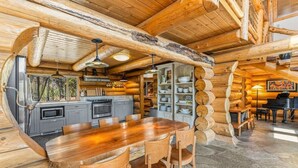 Ein rustikales Blockhaus-Interieur mit einem Holzespeisesaal, Stühlen, einer Küche mit grauen Schränken und einem Klavier.
