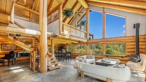 Ein Holzblockhaus-Interieur mit Steinboden, einem Klavier, einer Treppe, einem Sofa und einem Kamin.