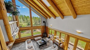 Ein geräumiger Raum mit Steinboden, Holzbalken, großen Fenstern, einem Kamin und einer Sitzecke mit Sofa und Sesseln.