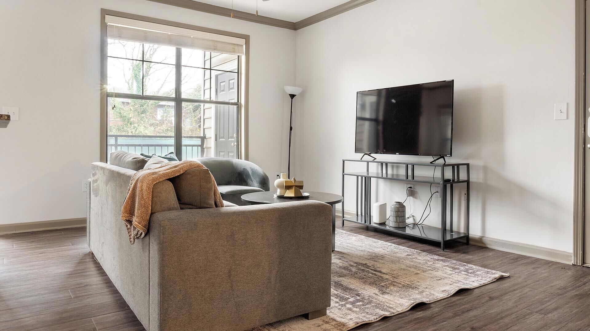 A living room with a sofa, a TV on a stand, a floor lamp, and a large window.