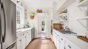 Cucina con mobili bianchi, frigorifero in acciaio inossidabile, piano cottura a gas e tappeto intrecciato.