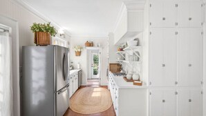Una cucina con mobili bianchi, un frigorifero in acciaio inossidabile, un pavimento in legno e un tappeto intrecciato.