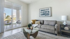 Ein Wohnzimmer mit Glastisch, einer Couch, einer Lampe und einem gerahmten Kunstwerk an der Wand.