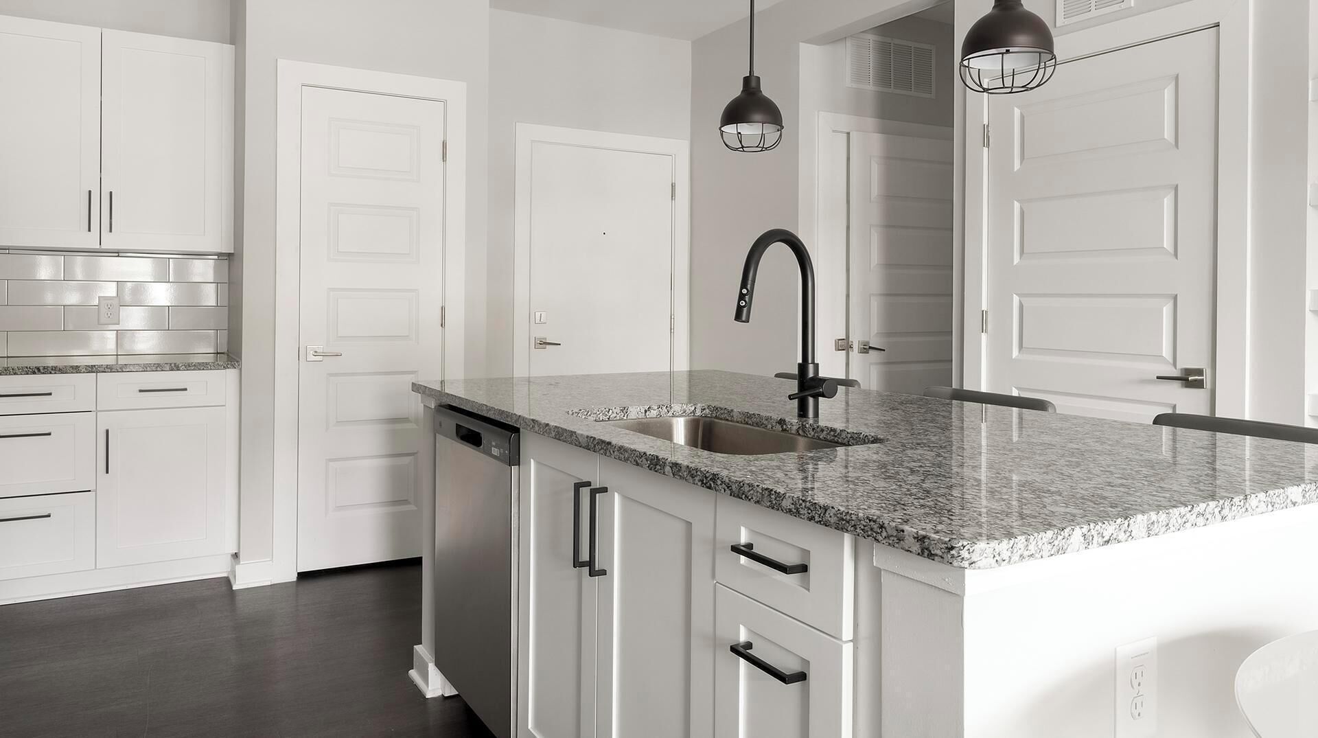 Una cocina con armarios blancos, encimera de granito, pileta de acero inoxidable y dos lámparas colgantes.