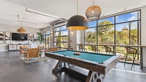 Ein moderner Poolbereich im Innenbereich mit Billardtisch, gemütlicher Sitzgelegenheit und großen Fenstern mit Blick ins Freie.