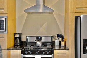 A modern kitchen with stainless steel appliances, a gas stove, a coffee maker, and wooden cabinets. - Orlando Retreat | 4BR Townhome • 8 Min to Disney (Osceola County)