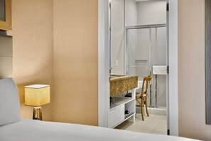 A hotel room with a bed, a bedside lamp, a bathroom with a shower, a sink, and a chair. - Orlando Retreat | 4BR Townhome • 8 Min to Disney (Osceola County)
