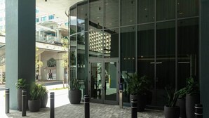 A modern building entrance with glass doors, potted plants, and a visible outdoor area with a staircase. - The Skyline Luxe Suite | 1BR+Den Downtown Miami (Miami)