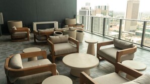A modern lounge area with multiple seating options, including sofas and chairs, arranged around small round tables. A large window offers a view of the cityscape. - The Skyline Luxe Suite | 1BR+Den Downtown Miami (Miami)