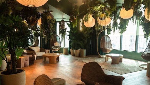 A spacious indoor area with a variety of seating options, including wicker chairs and a hanging chair, surrounded by large potted plants and hanging lanterns. - The Skyline Luxe Suite | 1BR+Den Downtown Miami (Miami)