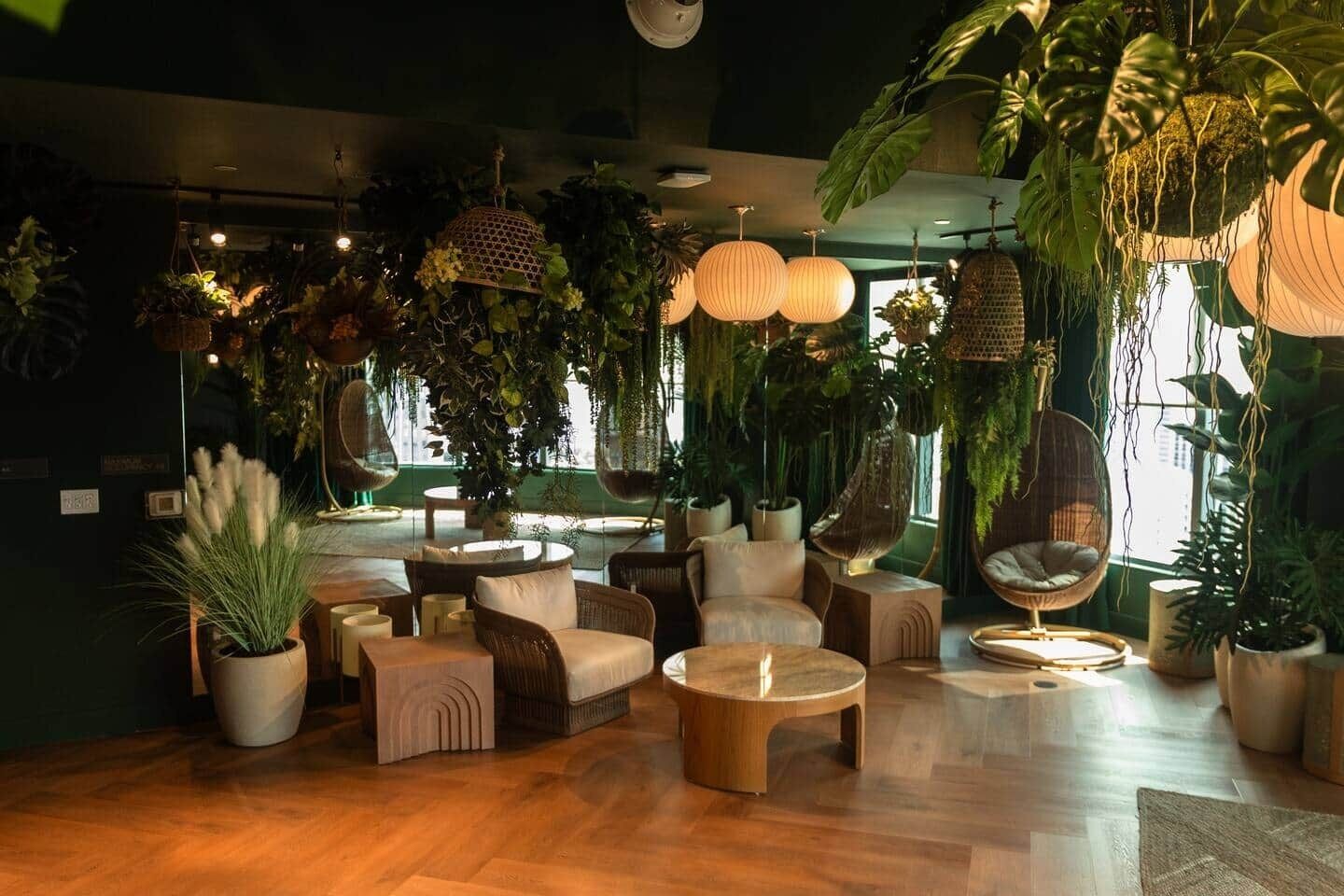A lounge area with round tables, cushioned seating, hanging plants, and pendant lights.
