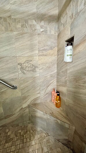 A shower area with a marble wall, a towel rack, and toiletries. - Cozy condo with a view of famous Kamaole Beach II (Kihei)