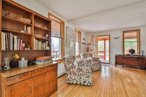 A spacious room with wooden flooring, a large bookshelf, two floral-patterned armchairs, and a wooden cabinet. - Hunter Mountain Home with Fire Pit & Deck (Hunter)
