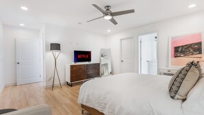 Een slaapkamer met een bed, een plafondventilator, een televisie, een dressoir en een deur.