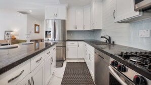 Een moderne keuken met witte kasten, roestvrijstalen apparatuur, een granieten aanrecht en een vloerkleed met patroon.